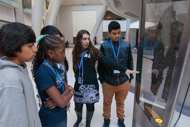 Instructor points to a Museum display and talks to a group of students.