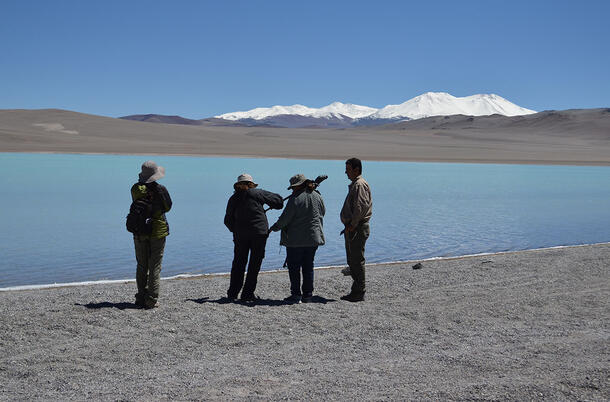 Four people stand near the water's edge to set up equipment.
