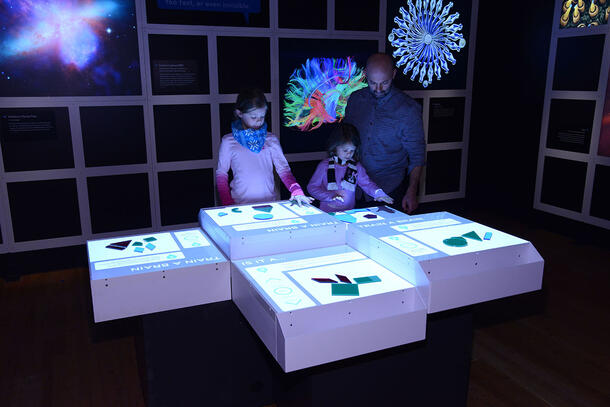An adult and two children use an interactive table in a darkened room.