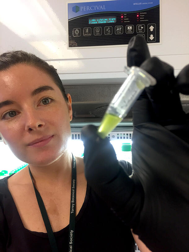 Paasch holds up a liquid specimen in a tube with a gloved hand.