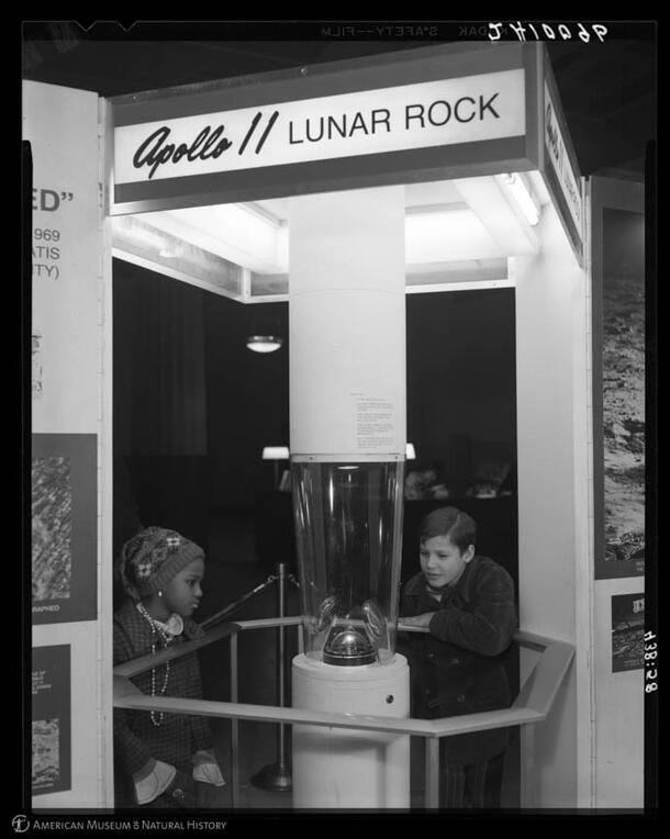 Two children look at a rock in a glass display case with a label reading Apollo II Lunar Rock.