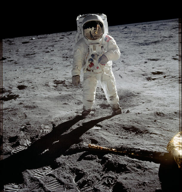 Neil Armstrong, fully enclosed in a bulky space suit and helmet, takes a step on the surface of the moon.