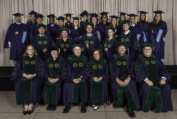 Graduates, faculty, Museum administrators, and the honoree in academic regalia pose for a photo.