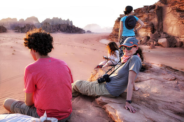 Rachel wears binoculars and a cap and rests on a rocky outcrop with some colleagues.