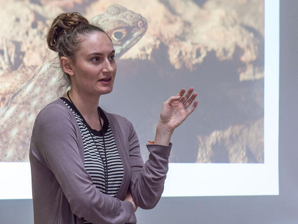 Rachel Welt speaks in front of a screen displaying an image of an iguana.