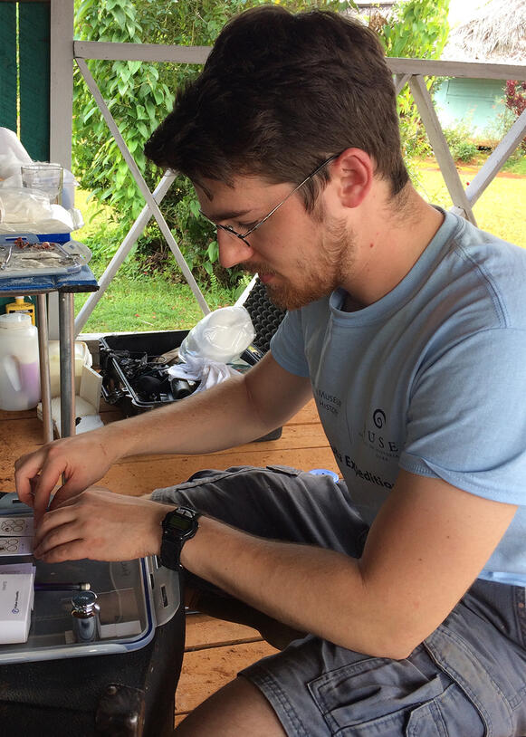 Spencer Galen prepares specimens at a small table, Humboldt National Park in Cuba is in view behind him.