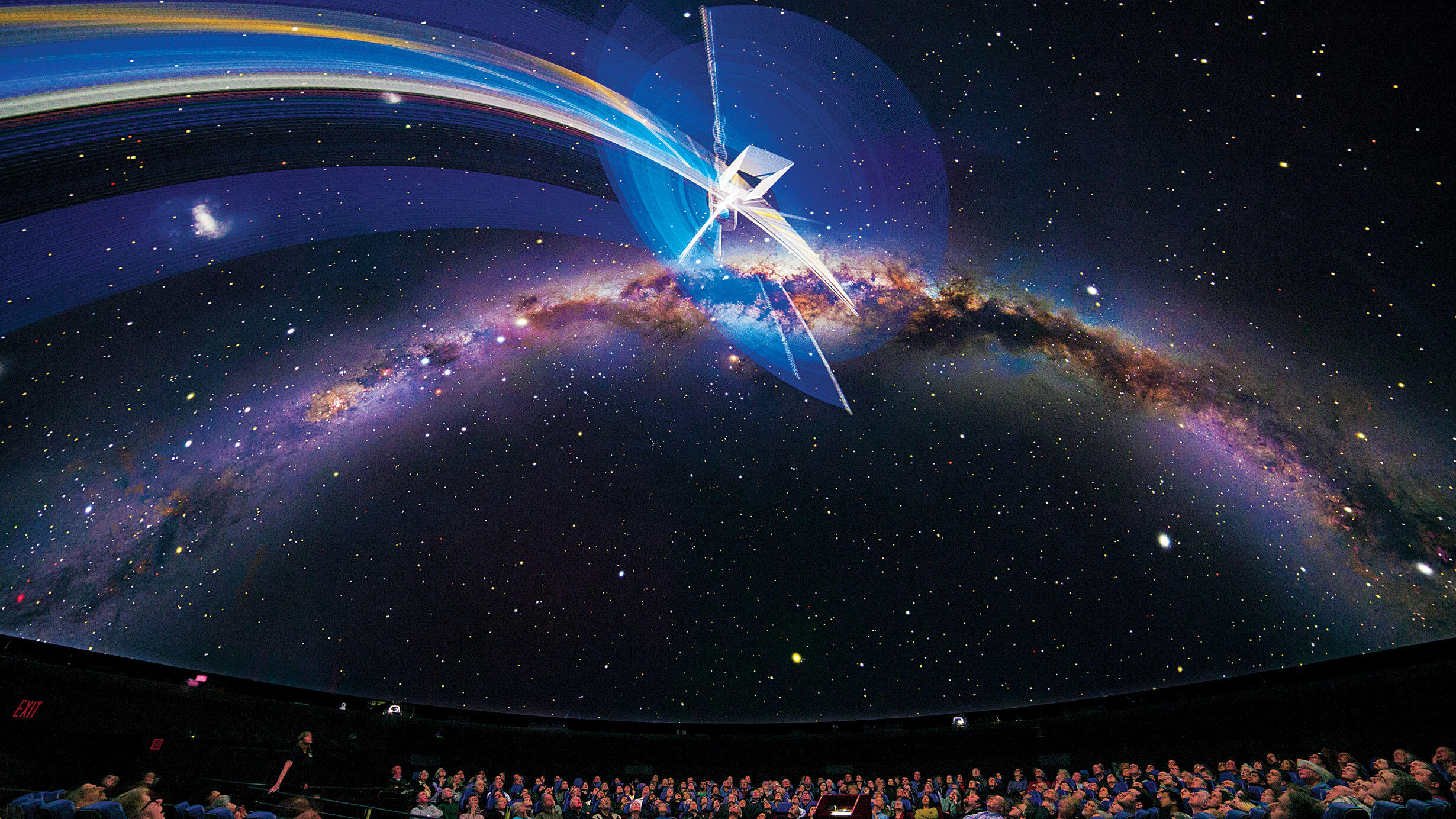 Visitors seated inside the Hayden Planetarium look up at the projections displayed on the curved overhead screen.