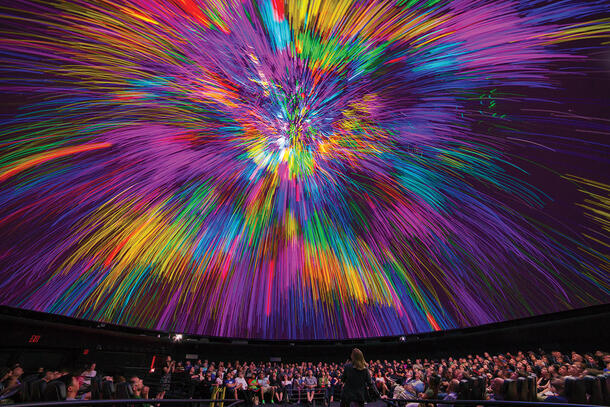 Visitors seated inside the Hayden Planetarium look up at the projections displayed on the curved overhead screen.