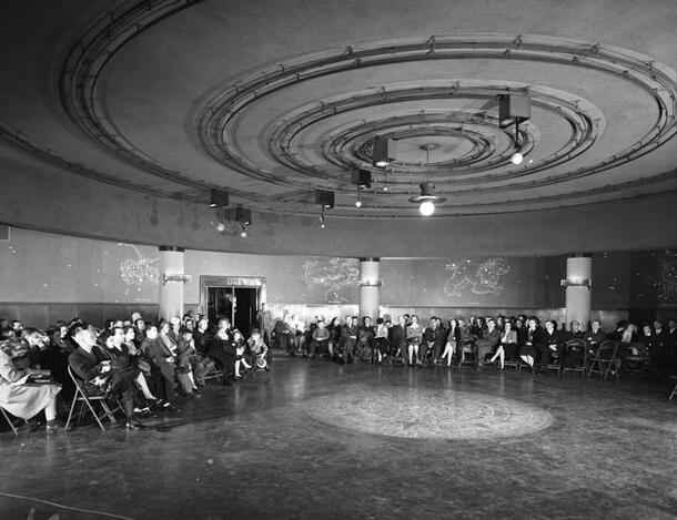 Hayden visitors seated in folding chairs gaze upwards at the display of the solar system.