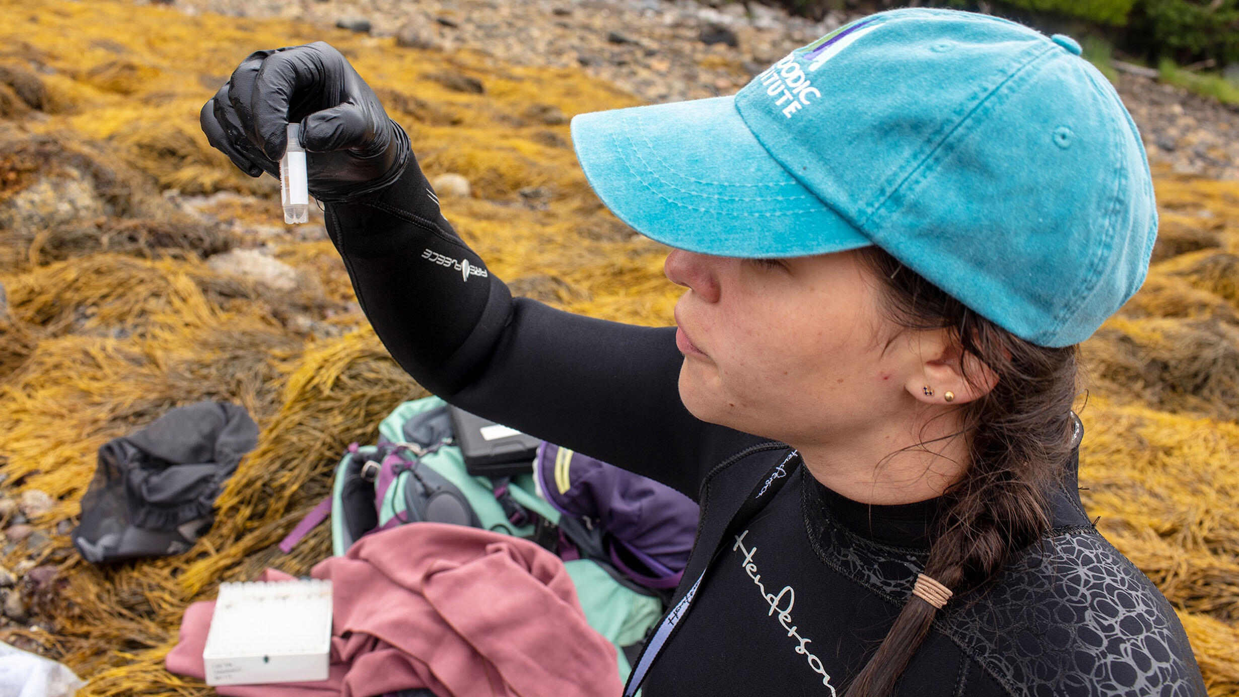 Scientist Melina Giakoumis, wearing a baseball cap and long-sleeve swimsuit, holds up a collections tube.