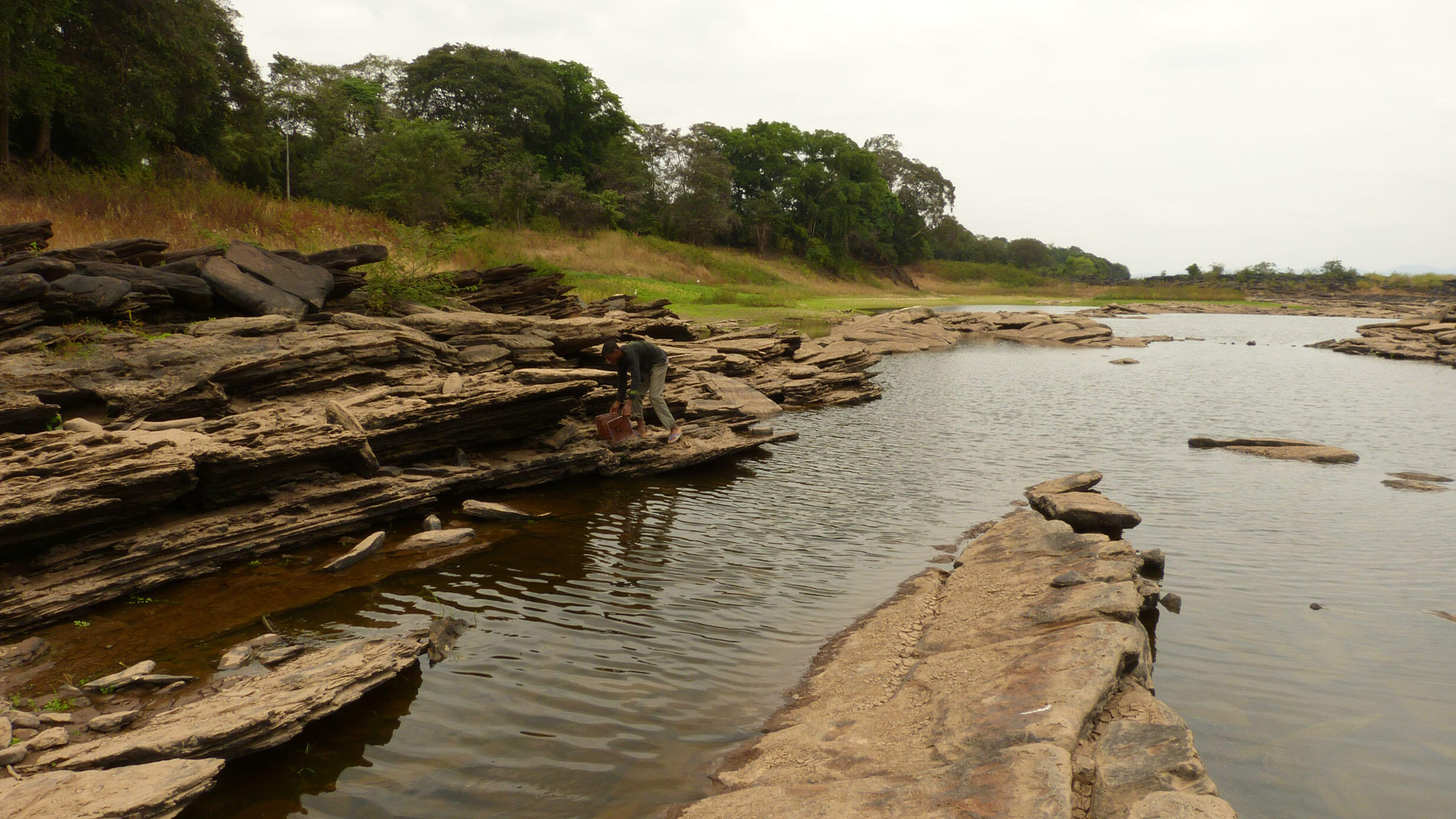 A person bends over along the jagged, rocky banks of the lower Congo River.