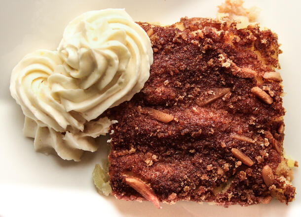 A square slice of an apple soufflé cake cockaigne with what seems like a dollop of sour cream icing next to it.