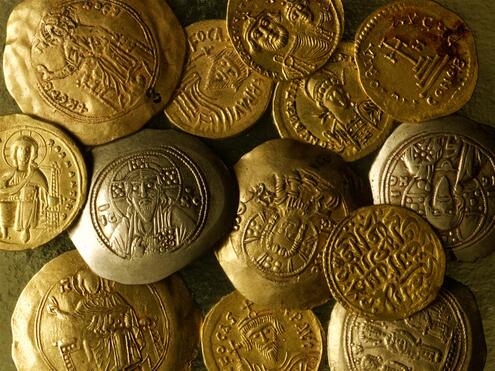 Closeup of 14 hammered gold coins inscribed with various signs, religious figures and text.