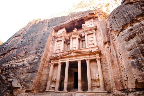 Sandstone mountain with façade of two-storied building carved away from its rock face. The building façade has many columns.