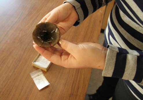 Hands of a woman holding a broken pottery cup that has been almost completely reassembled, except for a missing section along the rim. 