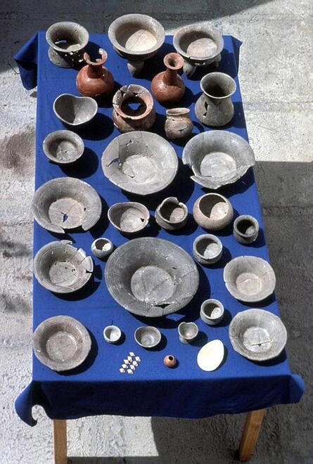 Overhead view of a table full of pottery artifacts. There are over 30 plates, bowls, cups and vases. 