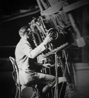 Black and white photo of Edwin Hubble looking through a large telescope at the Mt. Wilson Observatory