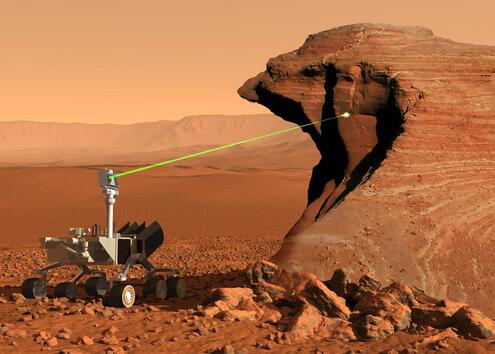 Curiosity rover (space rover with six wheels and a laser head) on a red rocky landscape. The laser is pointing a big rock.