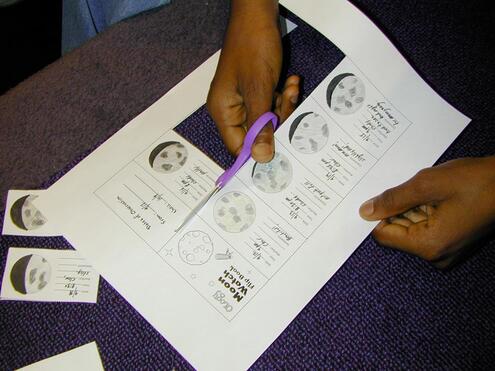 Close-up of a hand using scissors to cut paper along a dotted line