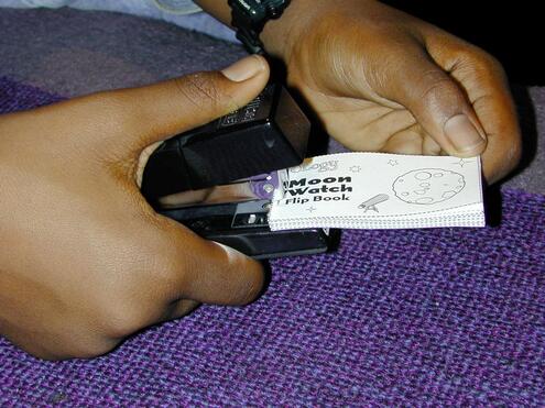 Close-up of hand stapling together small pieces of paper into a booklet. 