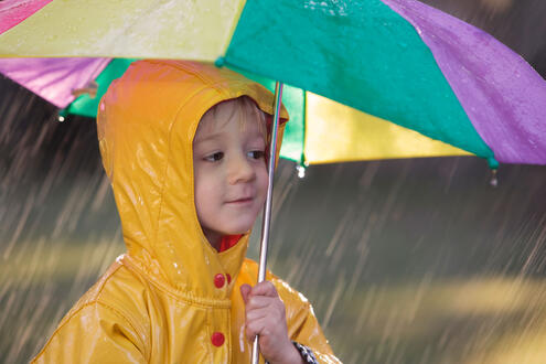 Young boy in raincoat shielding himself from rain with an umbrella.