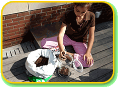 A child transferring soil with their hand from a bag into a small cylindrical clear container.