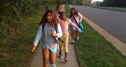 Kids happily walk on a sidewalk next to an empty road