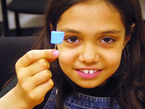 girl displaying the foam square with the needle poked through the middle