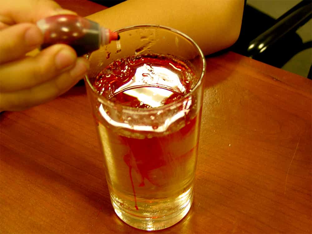 putting a few drops of red food coloring into glass with sugar and water mixture