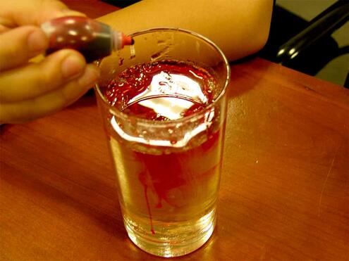 putting a few drops of red food coloring into glass with sugar and water mixture