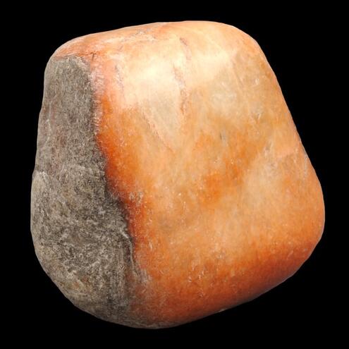 chunk of orange jade with one side unpolished, looking rough and brown