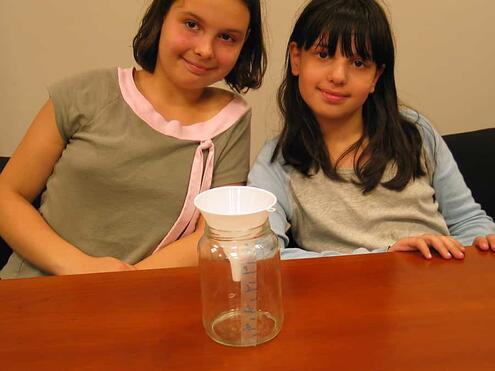 girls displaying final rain gauge jar with funnel inserted into opening
