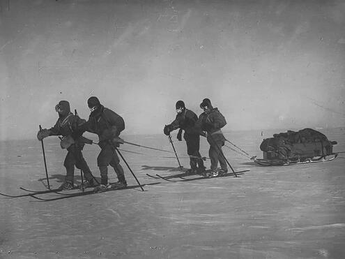 4 men on skis tethered to sled loaded with gear