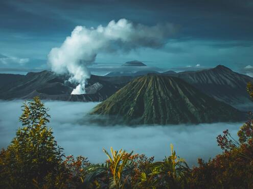Dark clouds hanging over a smoking volcano and mountain range.