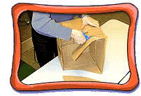 Person, with only their arms visible, uses scissors to cut diagonally across cardboard box to create diorama shape.