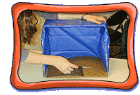 A person's two hands visible holding down a cardboard diorama box and taping sandpaper pieces to the bottom of the diorama.