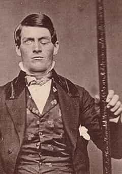 Phineas Gage, one eye closed due to an injury, seated and holding a tamping iron.