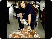Mark Norell bent over a fossil specimen of a nesting Oviraptor with one hand on the fossil, in his office.