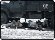 Three people lie beneath a truck in the desert.