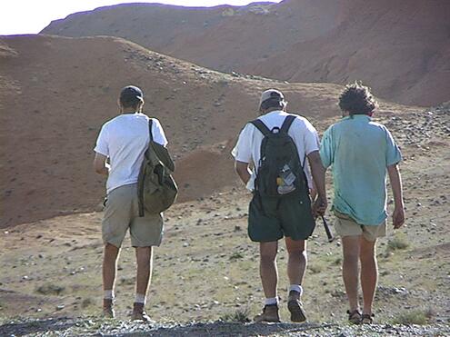 three expedition members walking towards hills