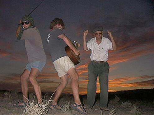 team member playing guitar at night with others dancing nearby