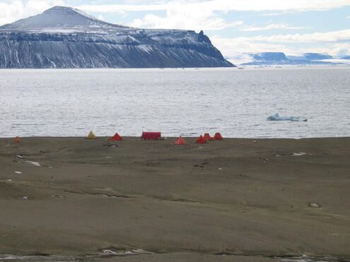 Group of tents by the water with floating ice and hills one the second term