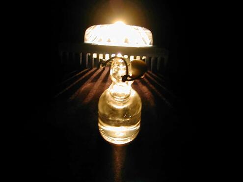a glass jar of oil in front of the light beams coming through the gaps between the teeth of the comb