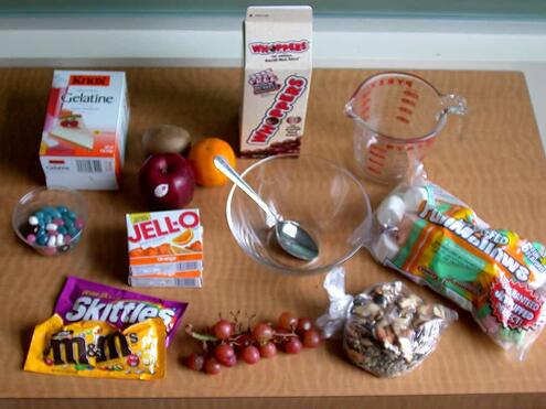 materials for activity including a bowl, spoon, jell-o mix, gelatin, measuring cup, marshmallows, jellybeans, and other candies
