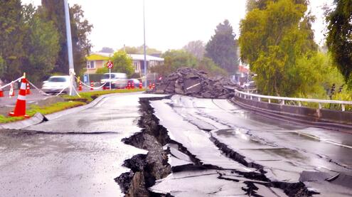 Deeply cracked paved road, with a large pile of rubble in the distance.