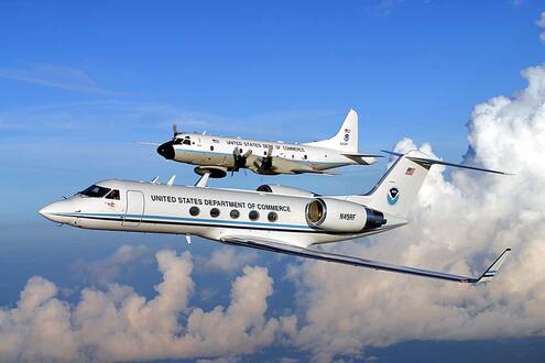 A jet plane with a smaller plane mounted on top, flying amid clouds. 