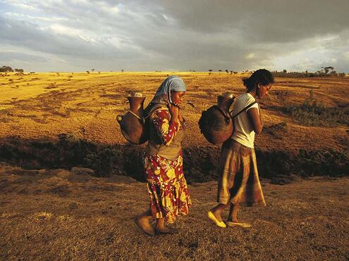 two women walking while carrying water