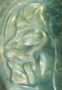 Close-up on a piece of jade with a stylized face carved into it.