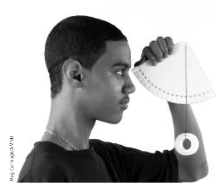 A young man, photographed in profile, holding a handmade astrolabe, constructed of paper and string, up to his face.