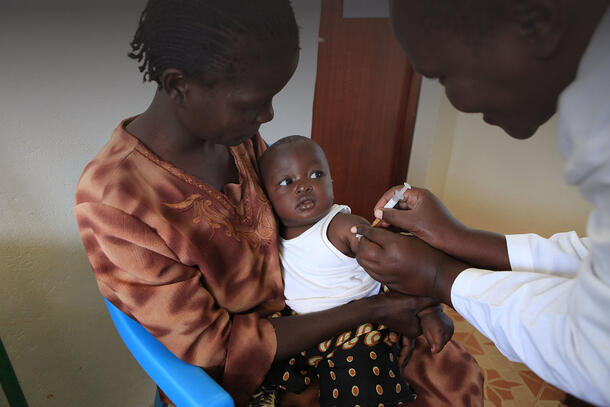 An infant carried by an adult receives a malaria vaccination via needle from a doctor.
